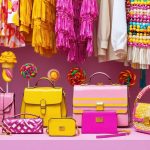 A vibrant selection of candy-colored fashion items, including clothing, accessories, and textiles, presented against an exotic travel market backdrop, portraying the trendy fusion of global influences and travel fashion.